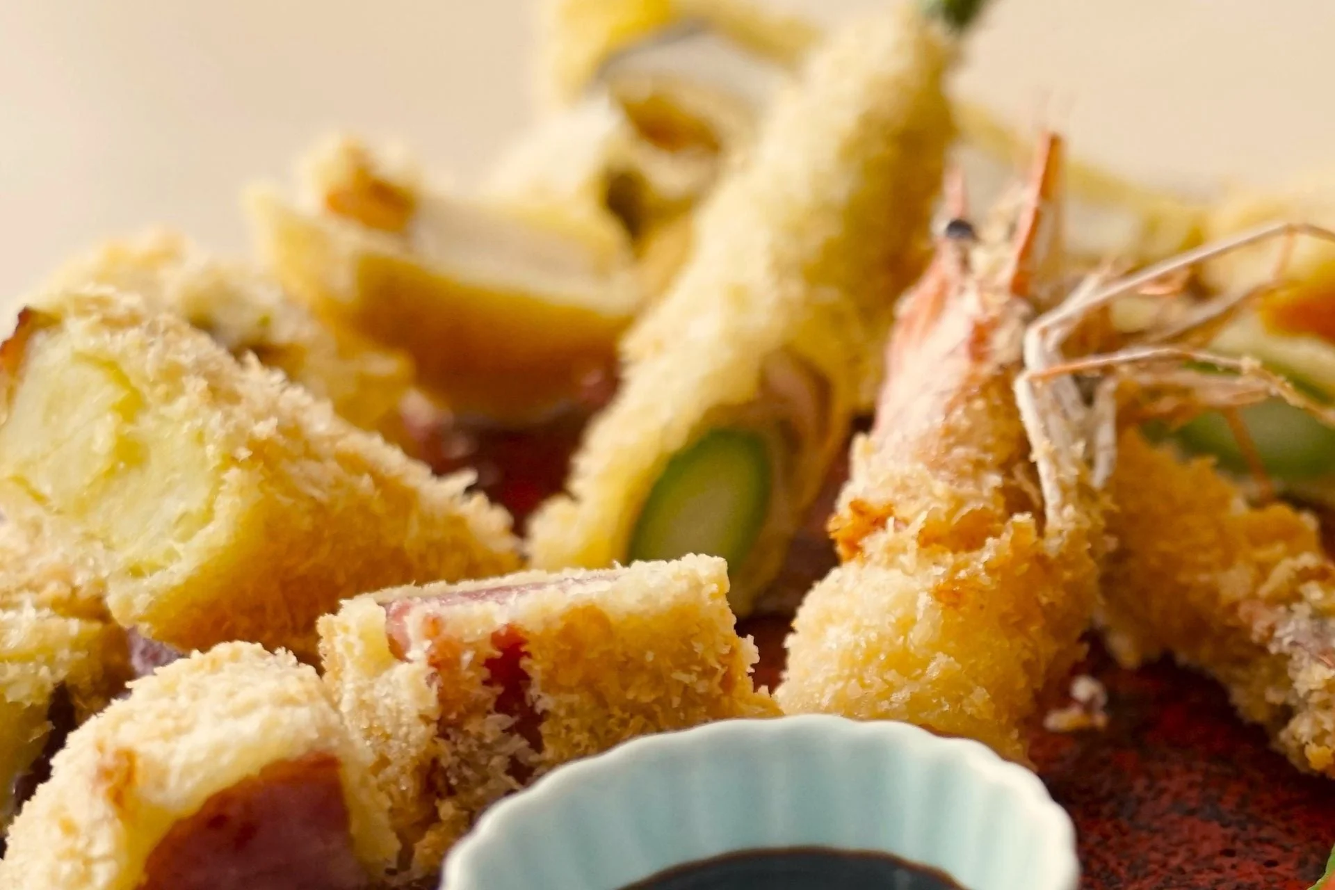 海老天や野菜の天ぷらなど、様々な揚げ物が美しく盛り付けられた和食のクローズアップ写真です。黄金色の衣が食欲をそそり、小皿のつけ汁が添えられています。