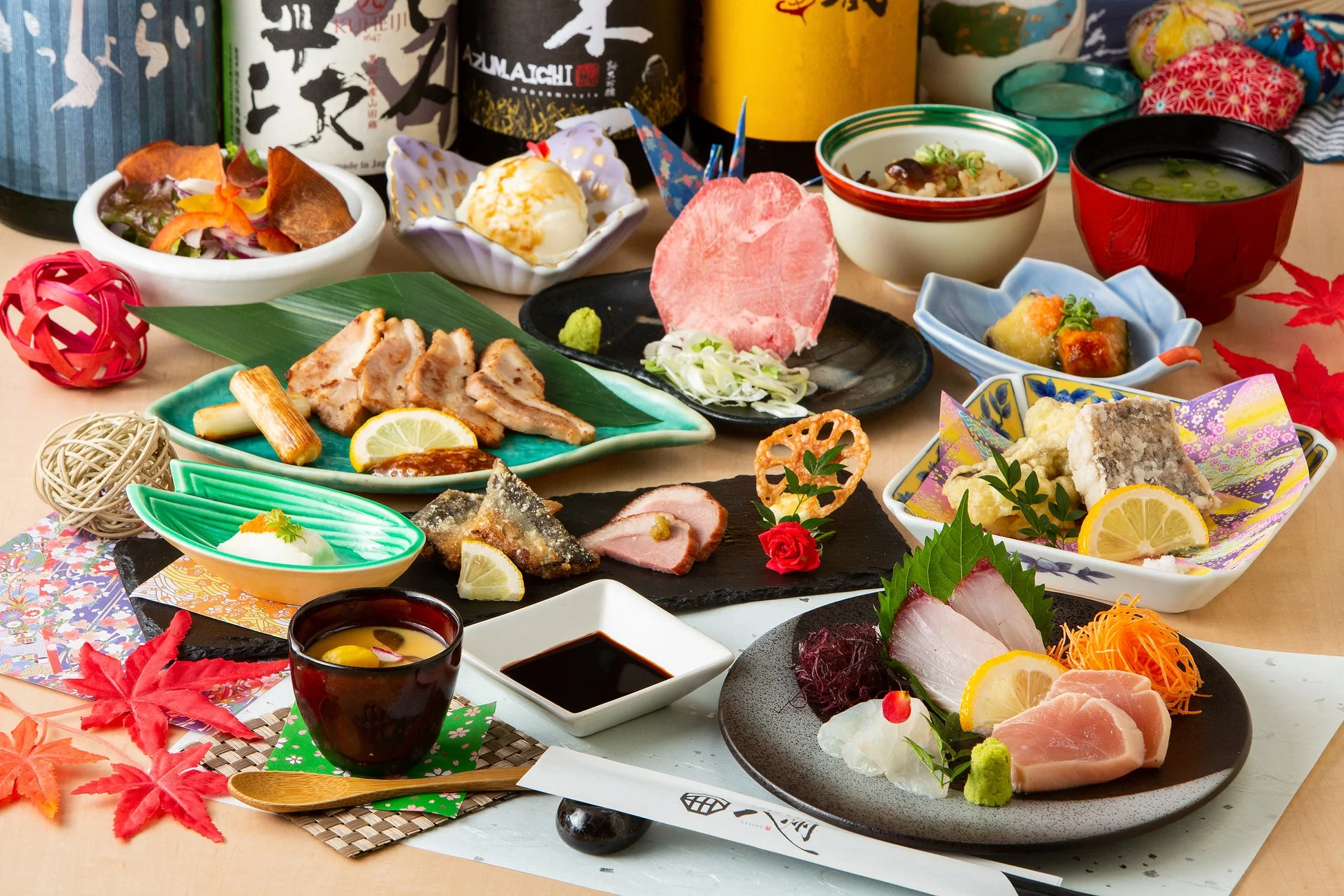 美しく盛り付けられた多様な和食が並ぶ豪華な食卓の様子。刺身や焼き物、小鉢料理などが彩り豊かに配され、日本酒の瓶や紅葉の飾りが添えられ、雅な雰囲気を醸し出しています。