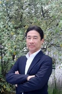 緑豊かな木々を背景に立つアジア系の男性