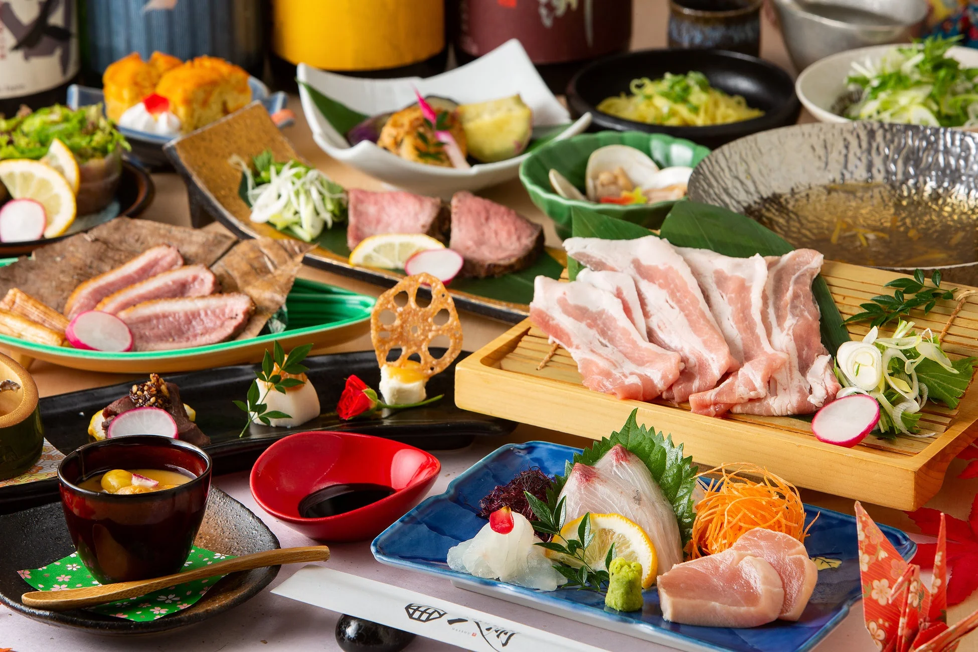 豪華な和食のコース料理が多数の器に盛り付けられ、テーブルいっぱいに並べられています。刺身、肉料理、煮物、小鉢など、彩り豊かで美しい品々が食欲をそそります。