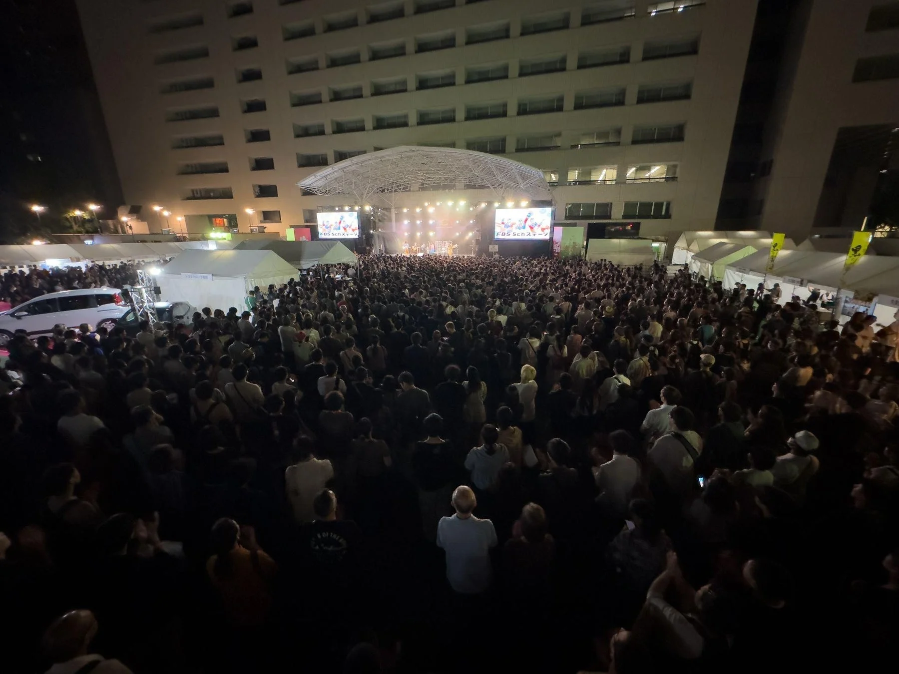 夜の屋外で開催されているライブイベントで、大勢の観客がステージを取り囲んでいます