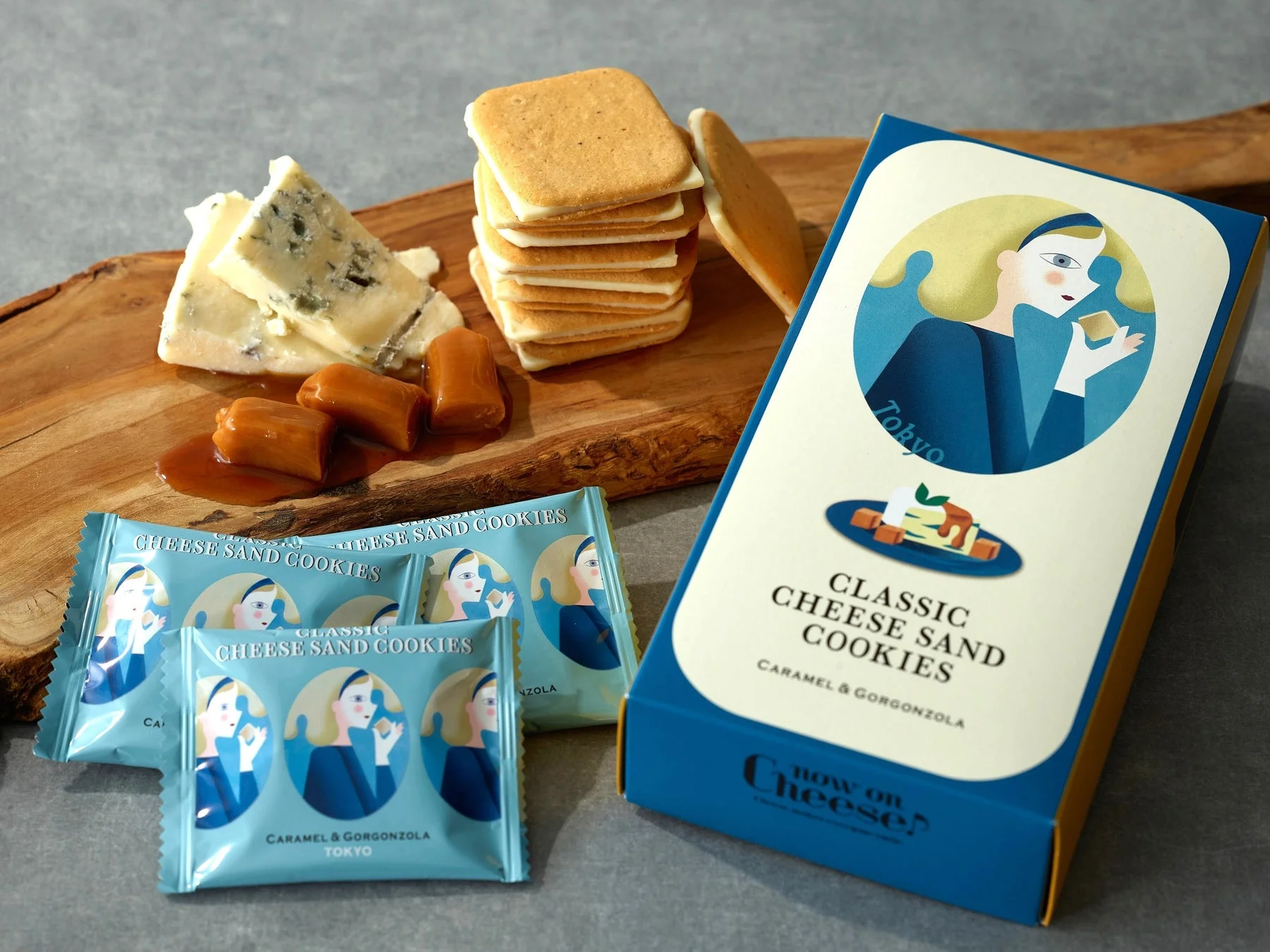 「Now on Cheese?」のキャラメル＆ゴルゴンゾーラチーズサンドクッキーのセット。青いパッケージの箱と個包装のクッキーが並び、ゴルゴンゾーラチーズとキャラメルが添えられている。