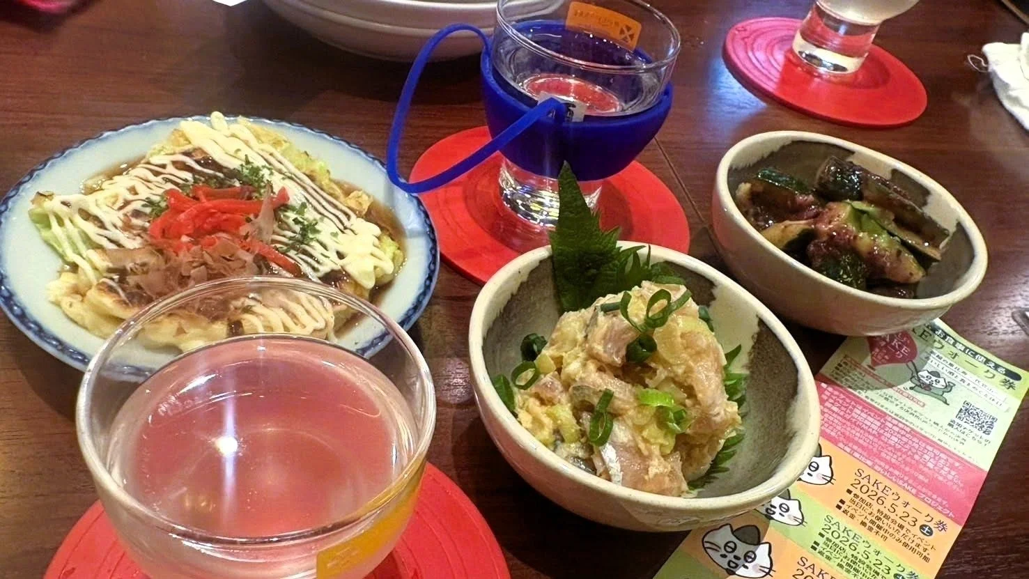 お好み焼き風の料理や小鉢のおつまみ、飲み物が並んだテーブルの様子