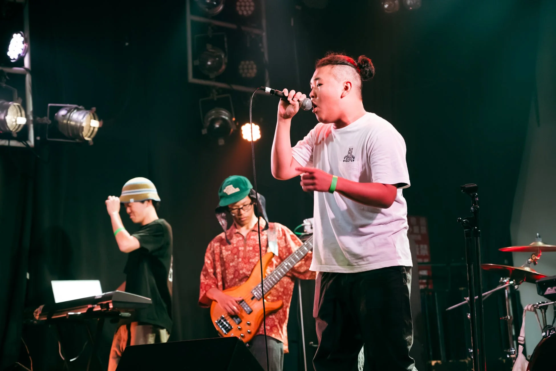 スポットライトが当たるステージで3人の男性がライブパフォーマンスを行っています。
