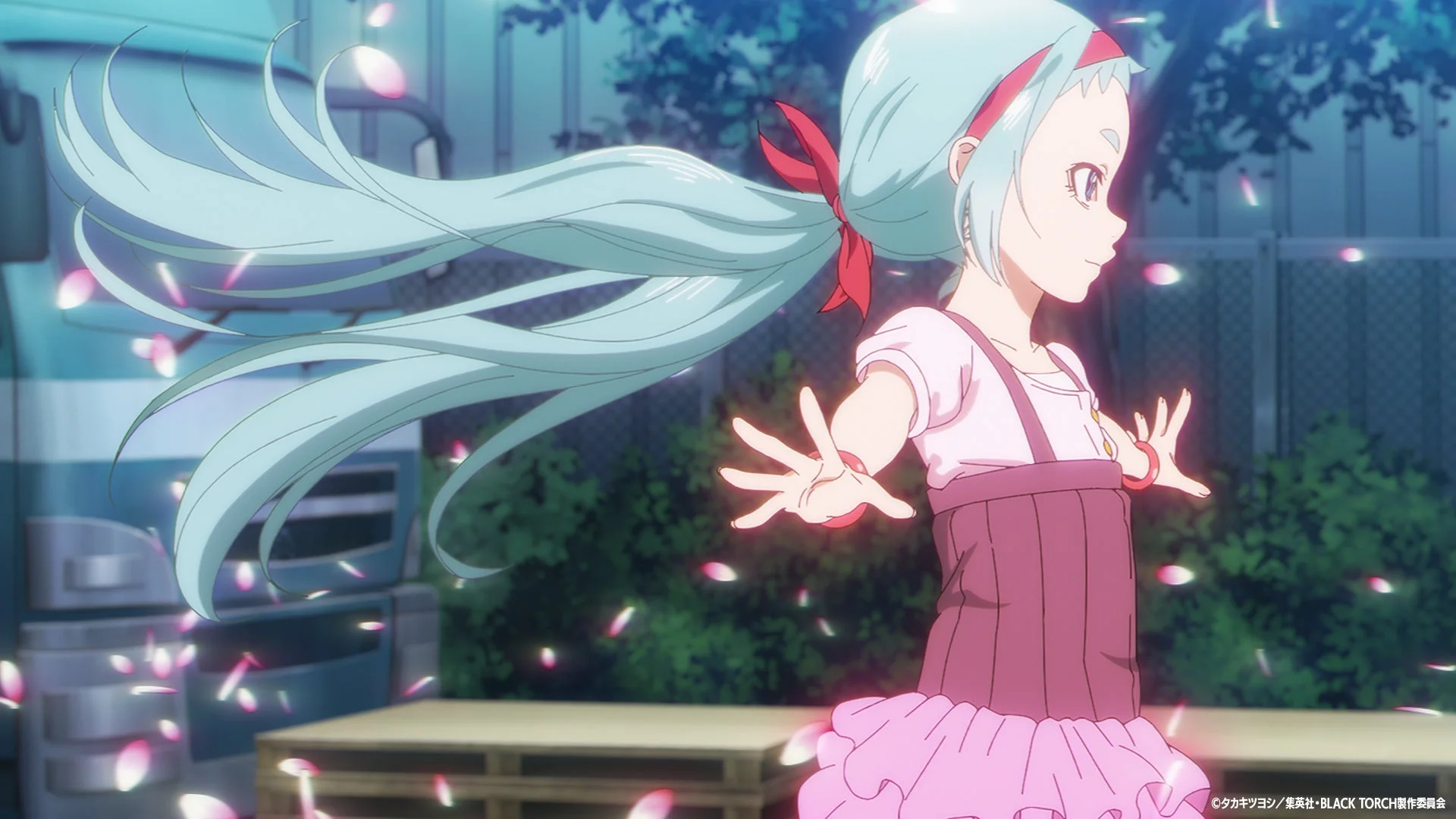 青い髪の少女がピンクの衣装をまとい、舞い散る花びらの中で両手を広げ、楽しげに踊っているようなアニメのシーン。夜の背景に幻想的な雰囲気が漂う。