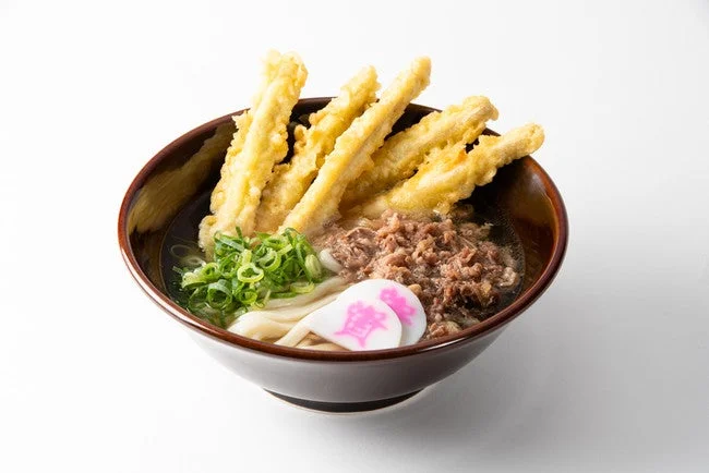 温かい出汁に浸かったうどんに、牛肉のしぐれ煮、青ネギ、なるとがトッピングされています。