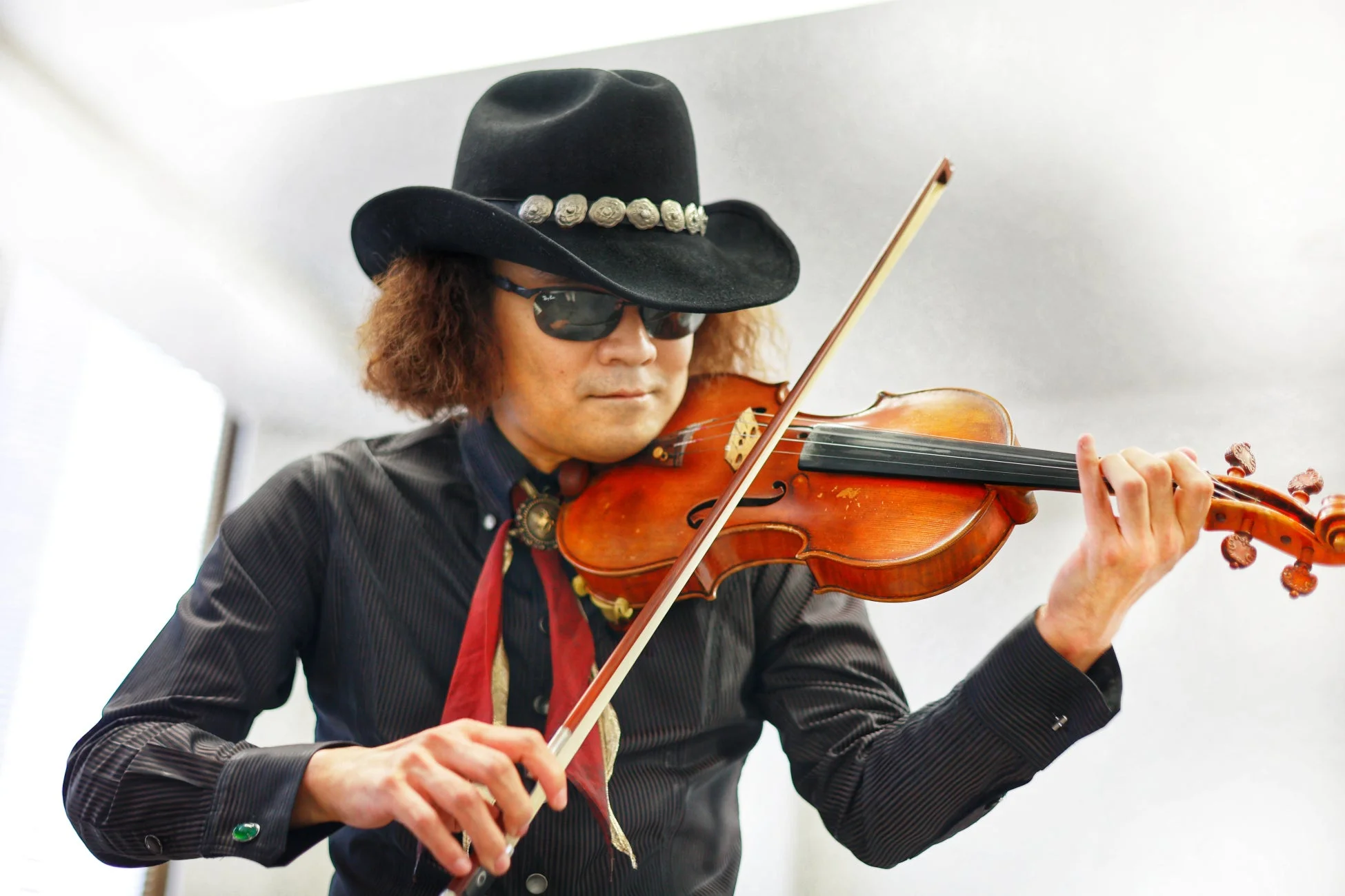 カウボーイハットとサングラスを着用した男性がバイオリンを演奏している様子を捉えた画像です。