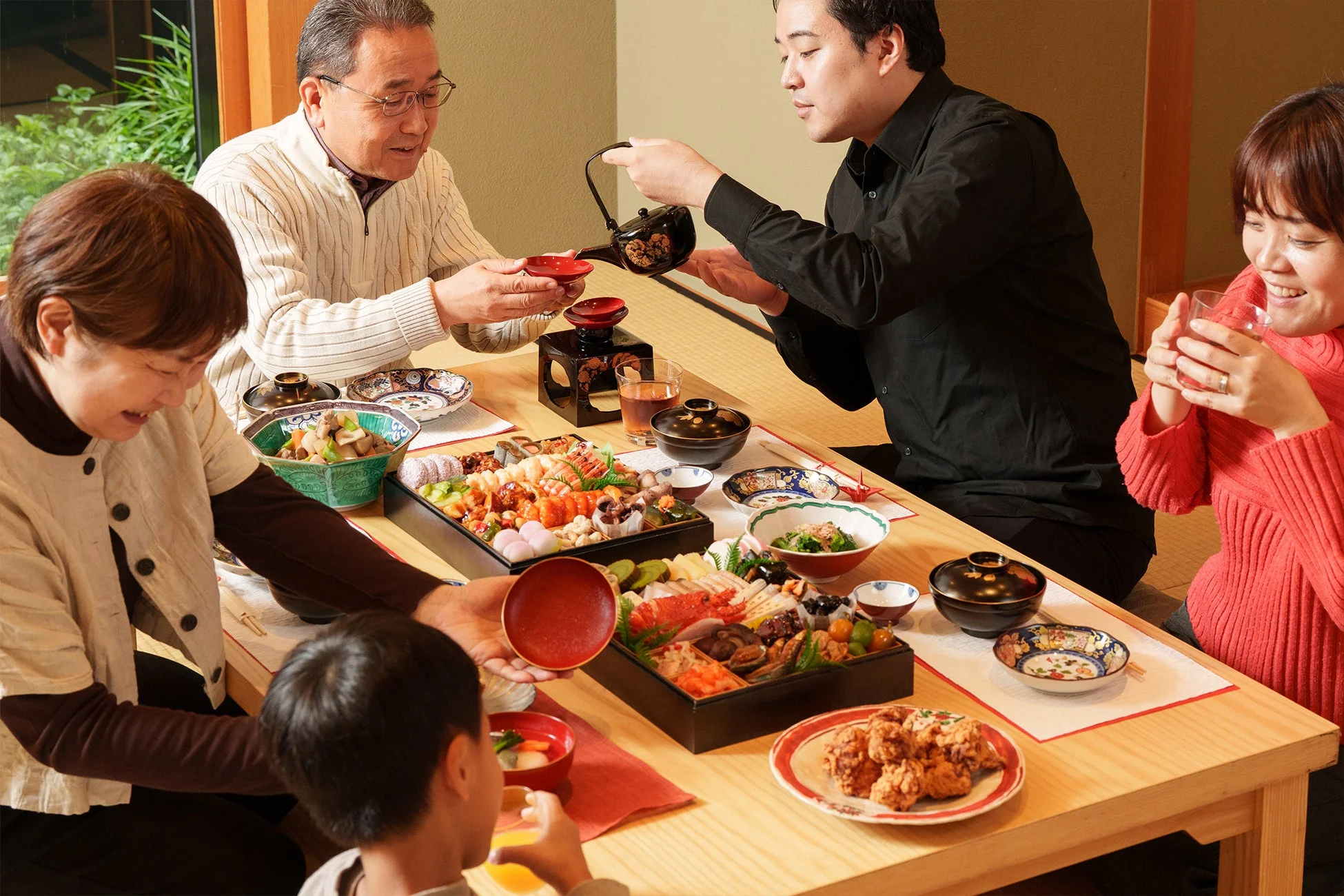 多世代の家族が和室のテーブルを囲み、豪華な日本料理を楽しんでいます。