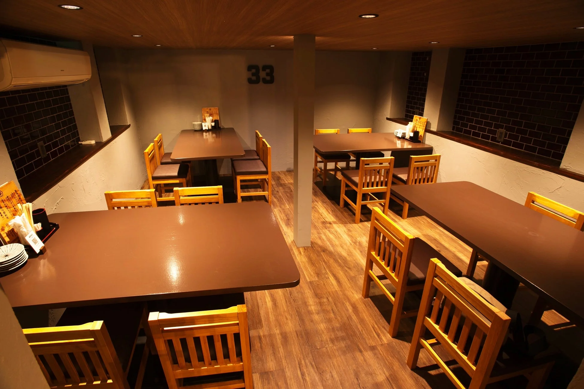 複数の茶色いテーブルと木製の椅子が並ぶ、落ち着いた雰囲気の飲食店内の様子