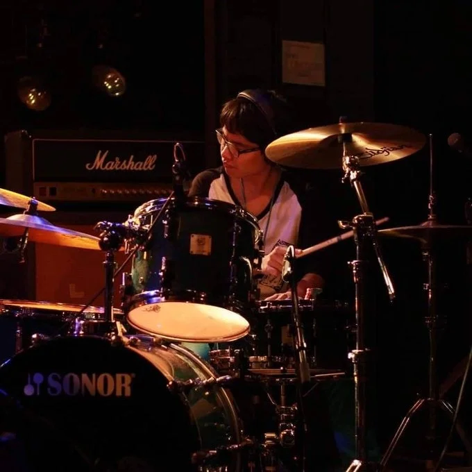 暗いステージでドラムを演奏している男性ミュージシャンの様子。