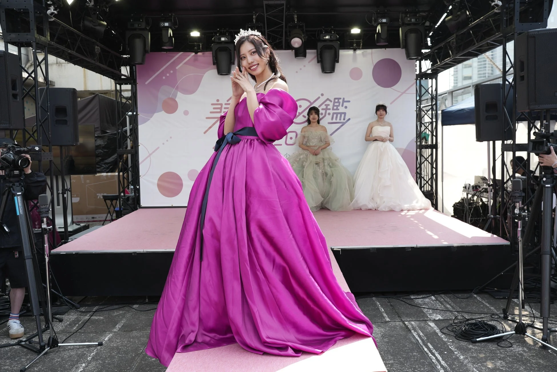 マゼンタ色の華やかなドレスを着た女性がステージ中央で笑顔でポーズをとる