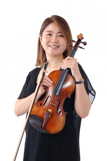 白い背景の前で、笑顔の女性がバイオリンと弓を抱えているポートレート。彼女は音楽家であり、楽しげな表情で楽器を構えている。