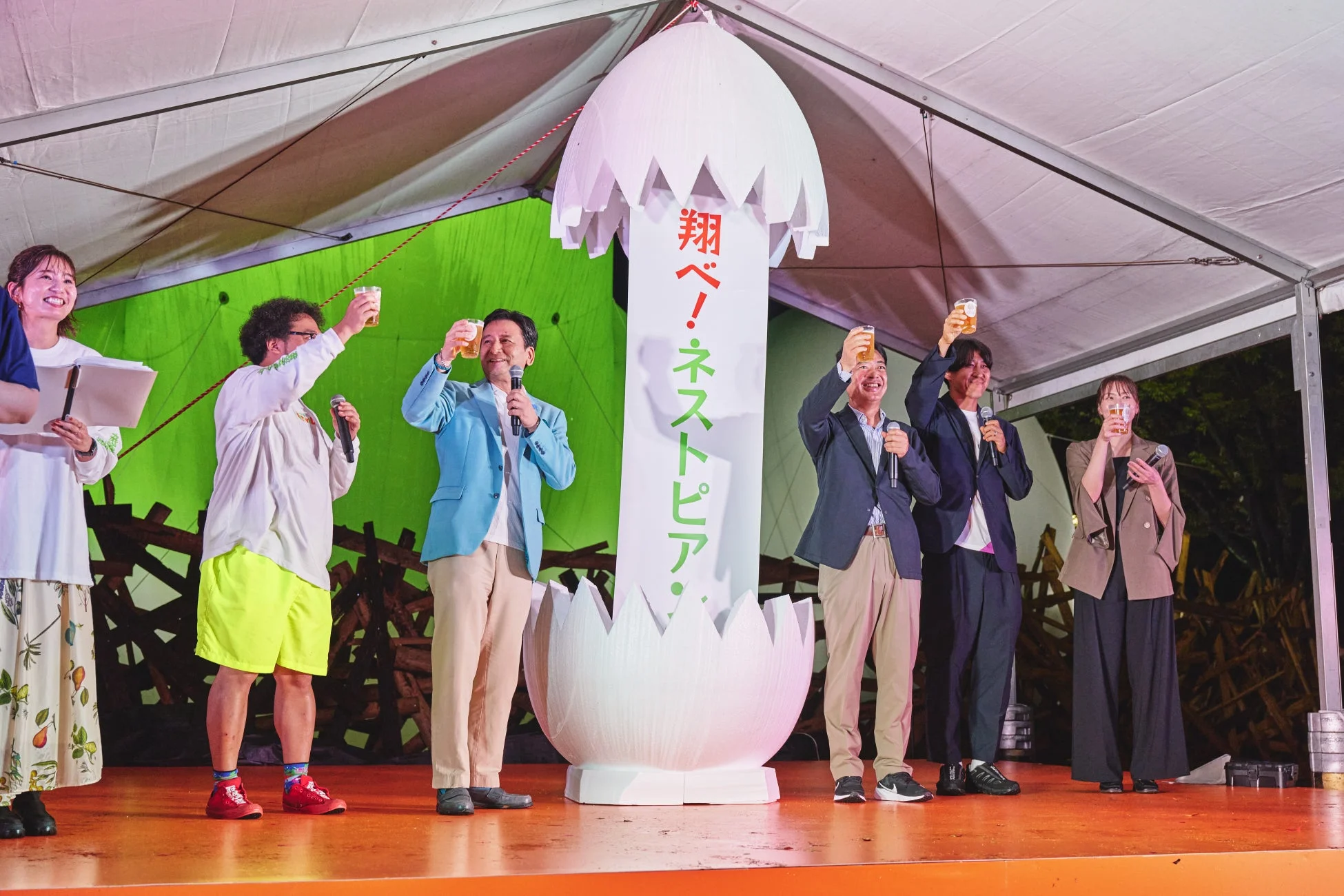 イベントステージで複数の男女がビールグラスを掲げて乾杯している様子