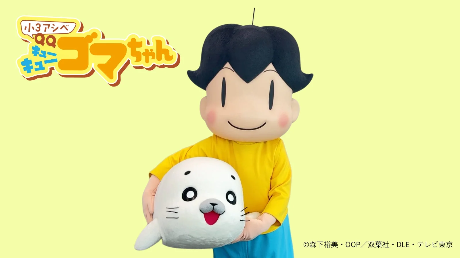 アニメ「少年アシベ GO! GO! ゴマちゃん」の主人公アシベの着ぐるみが、白いゴマちゃんのぬいぐるみを持っている画像。明るい背景で、可愛らしいキャラクターが特徴的です。