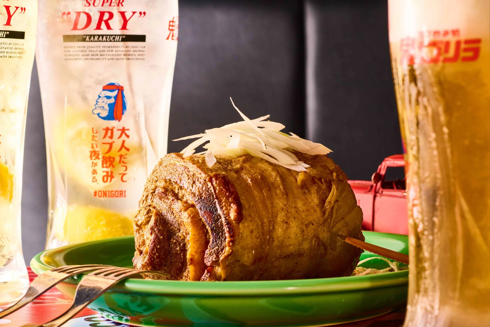 刻みネギが添えられた大きな肉料理とビール